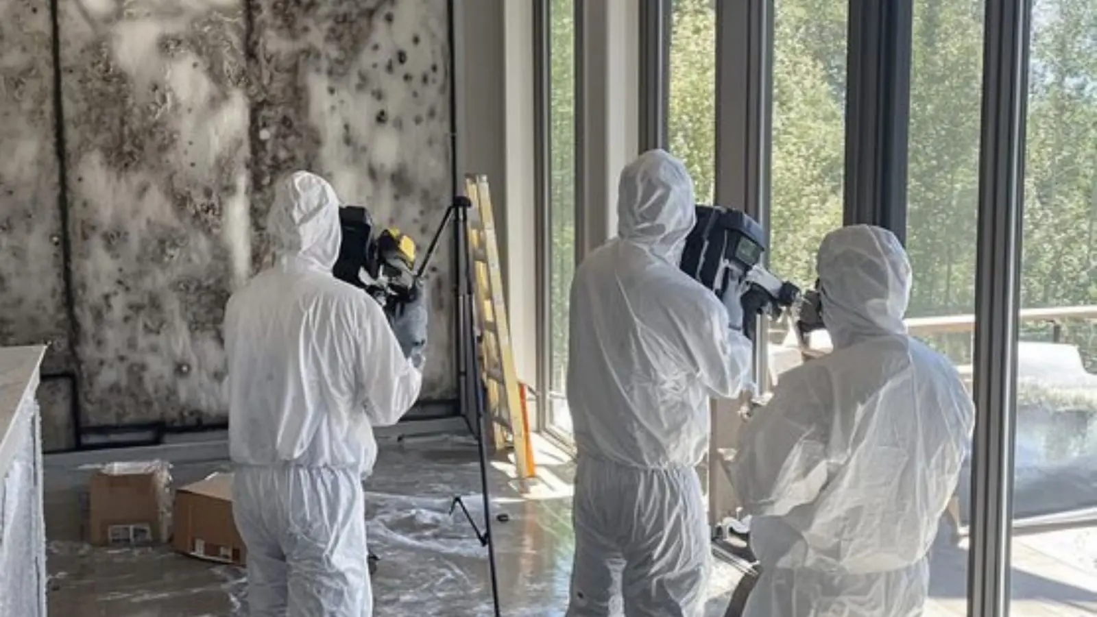 Inspectors in protective suits documenting a room with a camera on a tripod