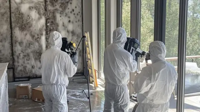 Inspectors in protective suits documenting a room with a camera on a tripod