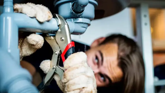 Plumber tightening a drain fitting under a sink with pliers